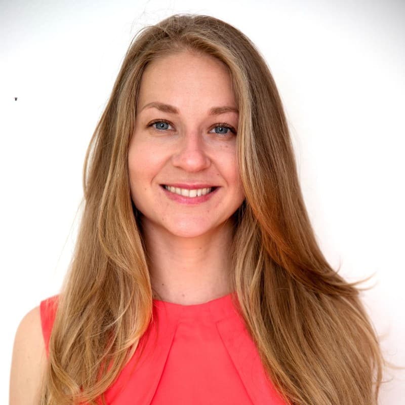 Smiling woman with long blonde hair and blue eyes wearing a vibrant coral top.